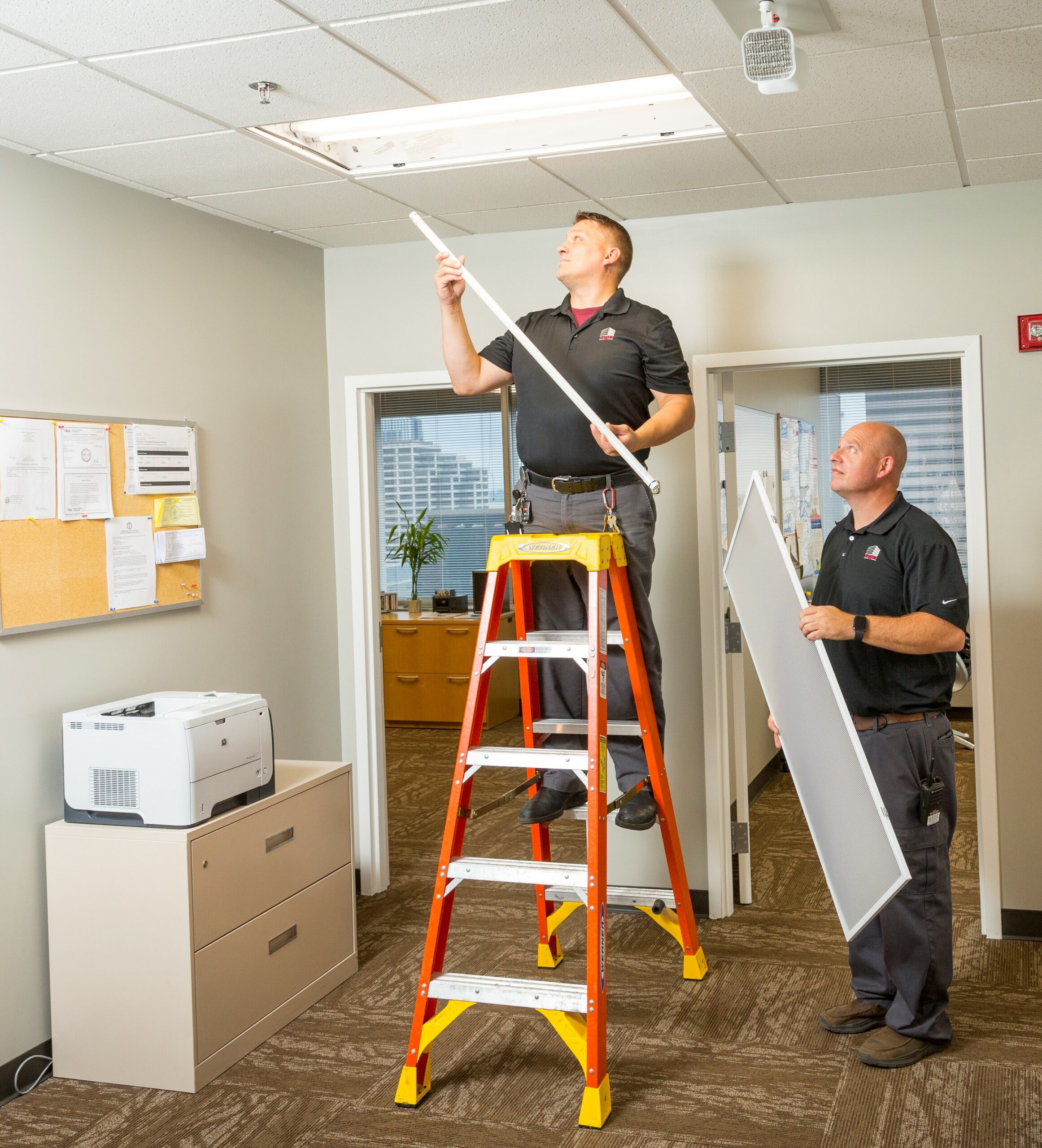 two men with ladder replacing a ceiling light.