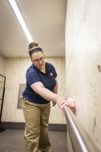 Day porter working for day porter services cleaning a handrail in an office hallway