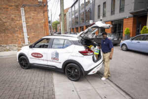 NSG Commercial Cleaning employee standing by company car with trunk open that has cleaning supplies in it