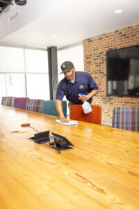 Commercial cleaning employee wiping table in office conference room while holding spray bottle