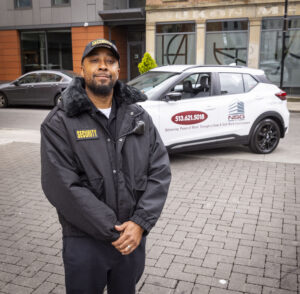 Security guard standing in front of patrol car and smiling at camera